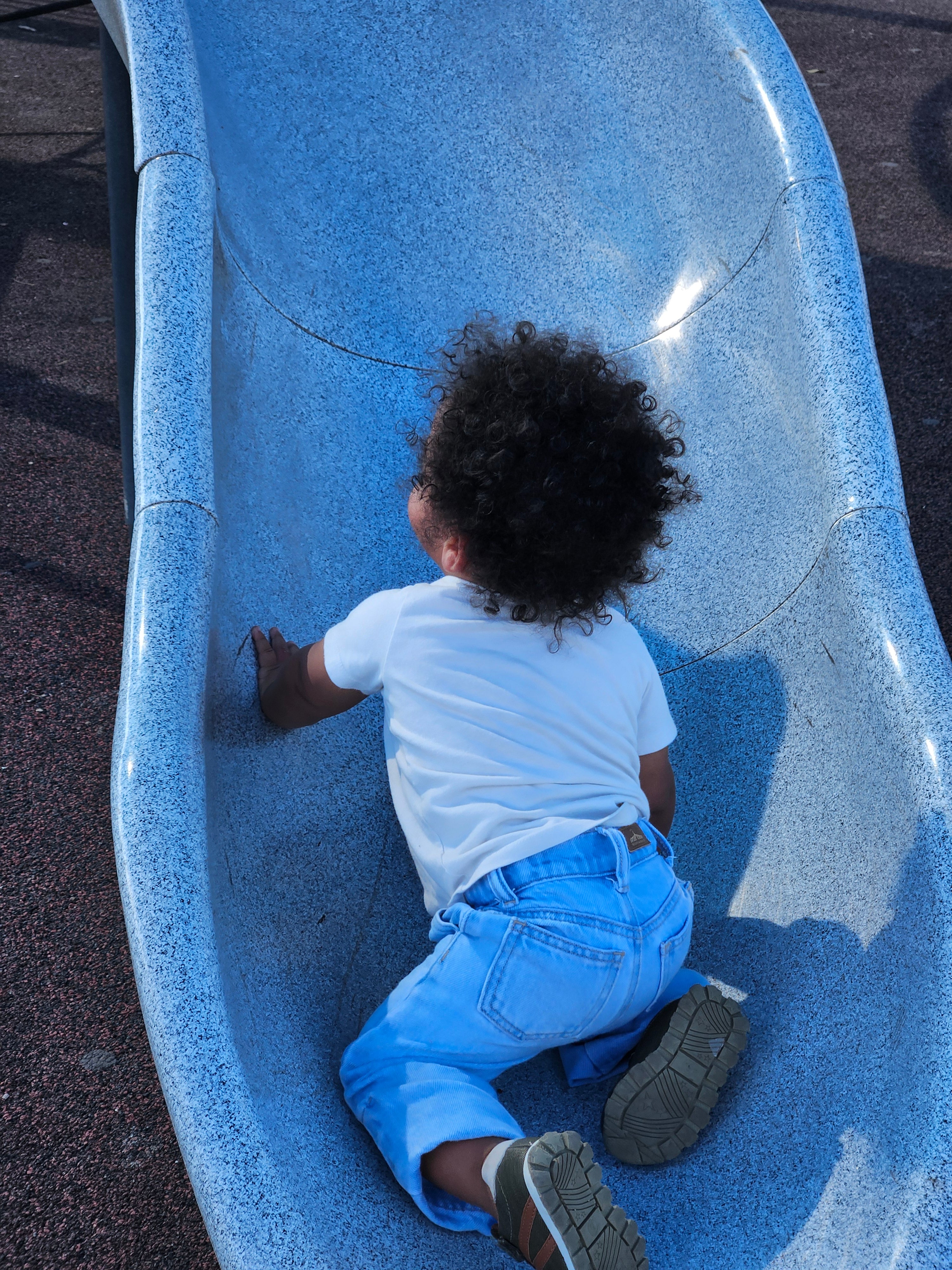 Child sliding down a blue slide at a playground i jeans