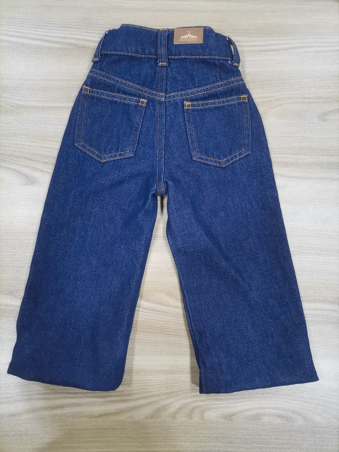 Rear flat lay of navy denim jeans on a wooden surface. Grow-Ease™ kids jeans showing shortest length of extendable hem feature that allows additional length as children grow