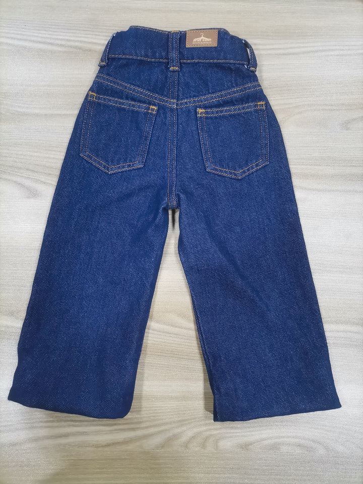 Rear flat lay of navy denim jeans on a wooden surface. Grow-Ease™ kids jeans showing shortest length of extendable hem feature that allows additional length as children grow